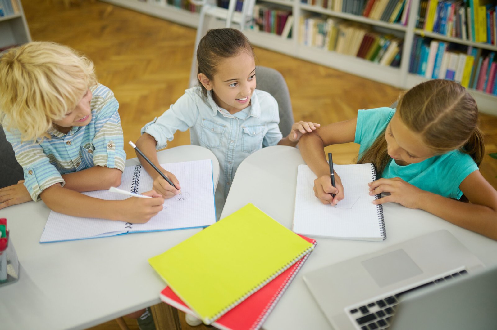 Top view of children writing at table in library